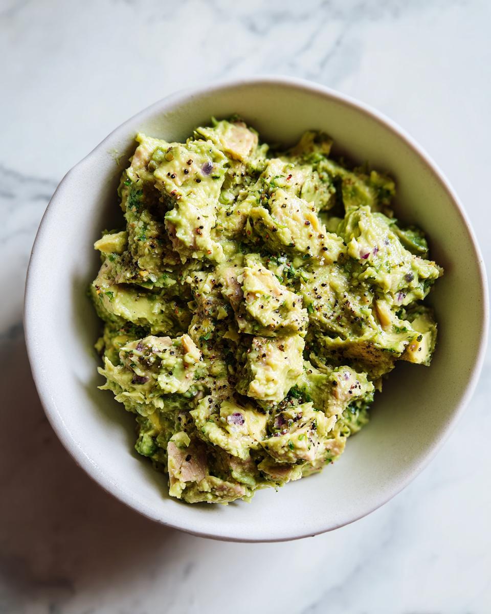 A bowl of creamy Avocado Tuna Salad with visible chunks of tuna, avocado, red onion, and herbs.