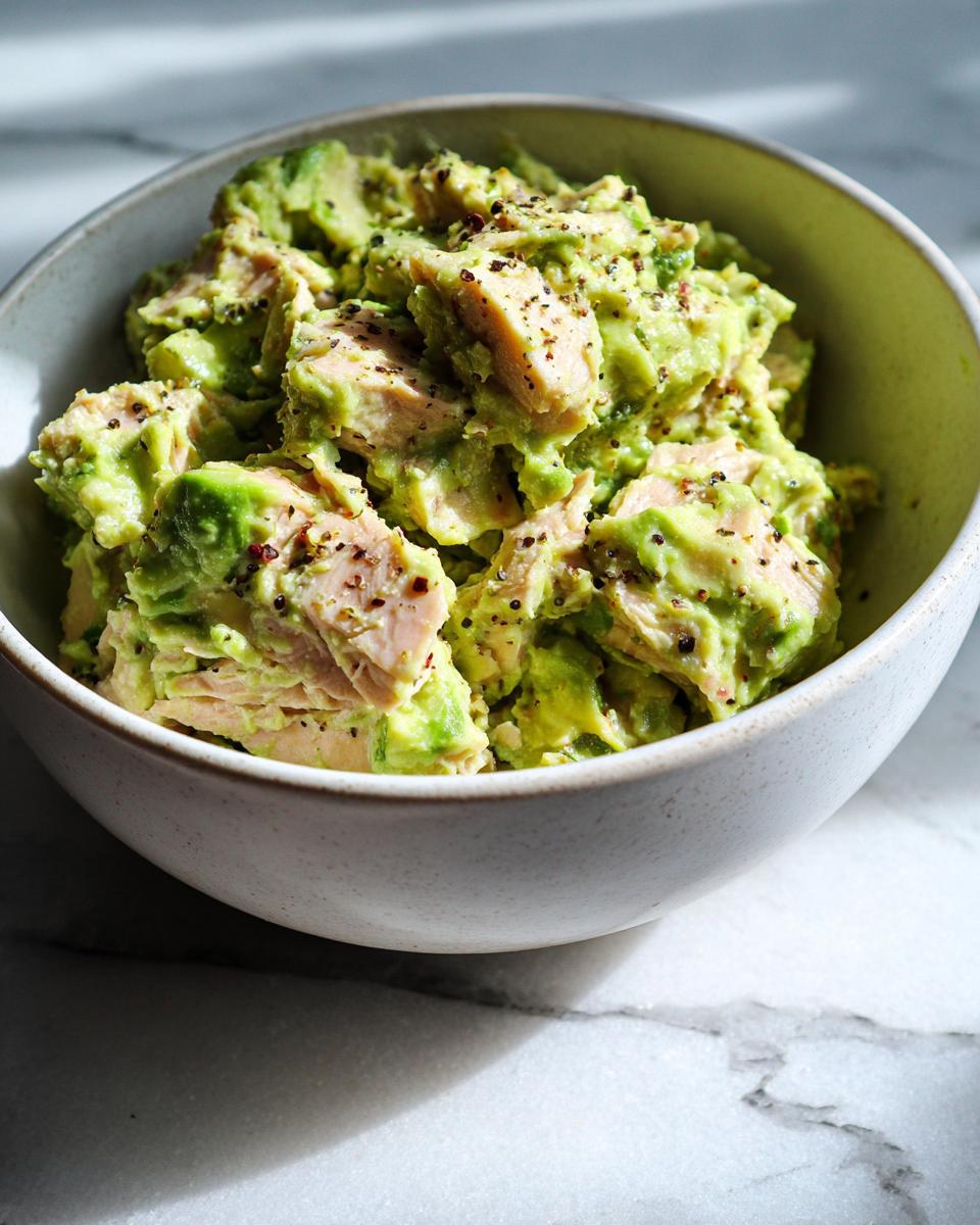 Close-up of a bowl filled with creamy Avocado Tuna Salad, seasoned with cracked pepper.