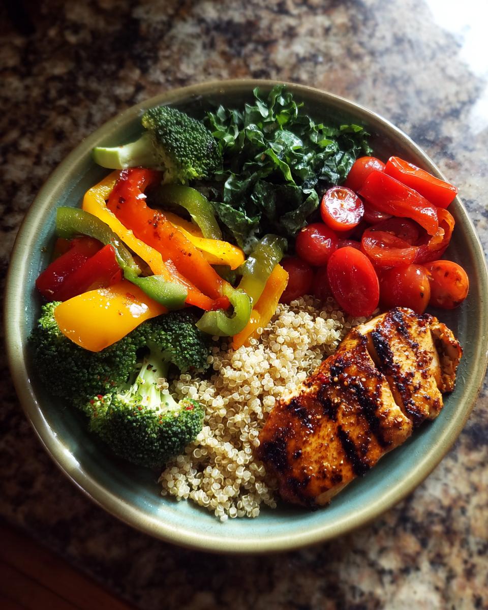A balanced weight loss plate featuring grilled chicken, quinoa, broccoli, peppers, kale, and tomatoes.