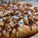 Close-up of a delicious BBQ Chicken Pizza with Red Onion, featuring melted cheese, shredded chicken, and a drizzle of BBQ sauce.