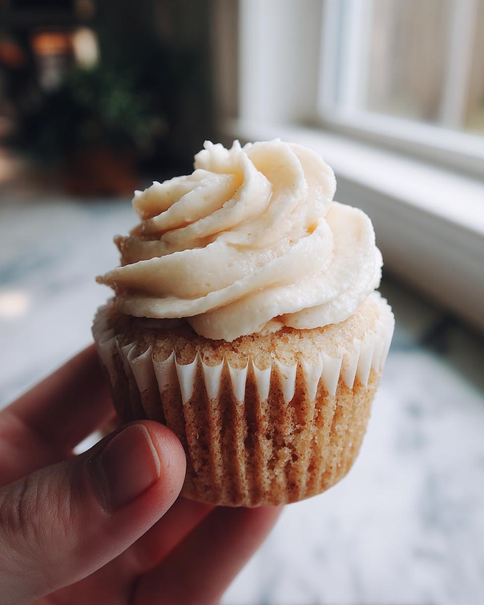 A hand holds a freshly baked birthday cupcake with creamy white frosting, ready to be enjoyed.