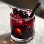 A glass of spooky Black Magic Sangria filled with dark berries, ice, and garnished with a blackberry and cherry.