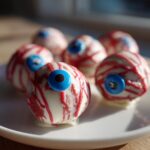 A plate of white chocolate-covered cake pops decorated to look like bloody eyeballs, perfect for Halloween.
