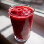 A glass filled with a vibrant red cherry vibe smoothie, showcasing its thick and refreshing texture.