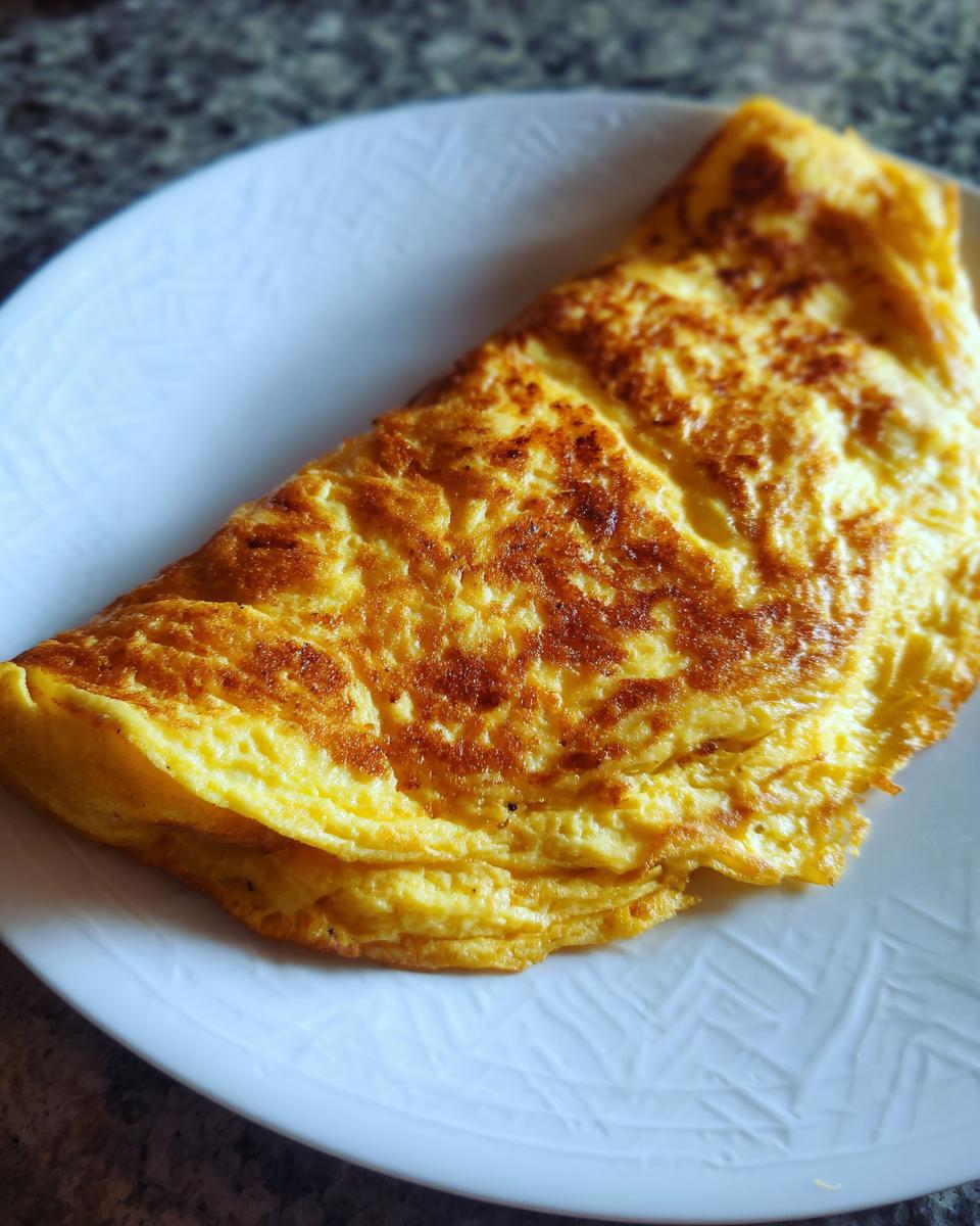 A golden brown, folded omelet sits on a white plate, ready to be enjoyed. Quick and easy omelet recipe.