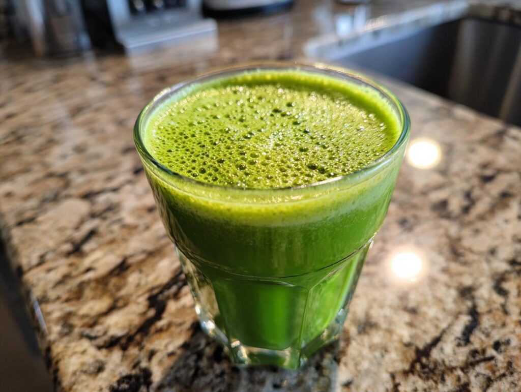 A glass of vibrant green Detox Drinks & Smoothies on a kitchen counter.