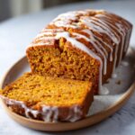 A slice of moist Maple Glazed Pumpkin Loaf, drizzled with white glaze, on a platter.