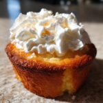 Close-up of a mini tres leches cupcake topped with whipped cream and a bite taken out.