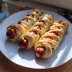 Three Mummy Hot Dogs wrapped in pastry with cheese eyes, ready for a Halloween party.