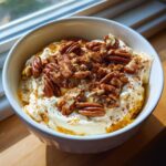 Bowl of pumpkin yogurt topped with pecans and cinnamon, a delicious high protein fall snack.