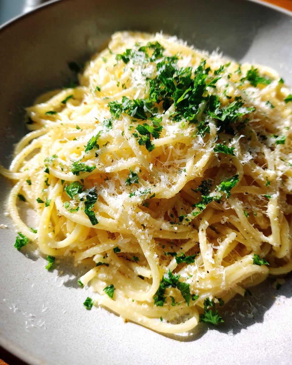 Close-up of spaghetti coated in a creamy sauce, topped with fresh parsley and grated cheese.