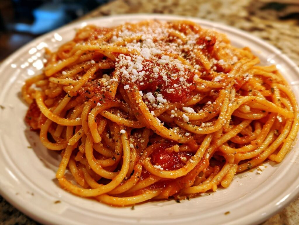 A plate of spaghetti with tomato sauce and grated cheese, showcasing a simple pasta recipe.