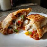 A close-up of a halved Veggie Supreme Pizza Pocket, overflowing with melted cheese, mushrooms, and bell peppers.