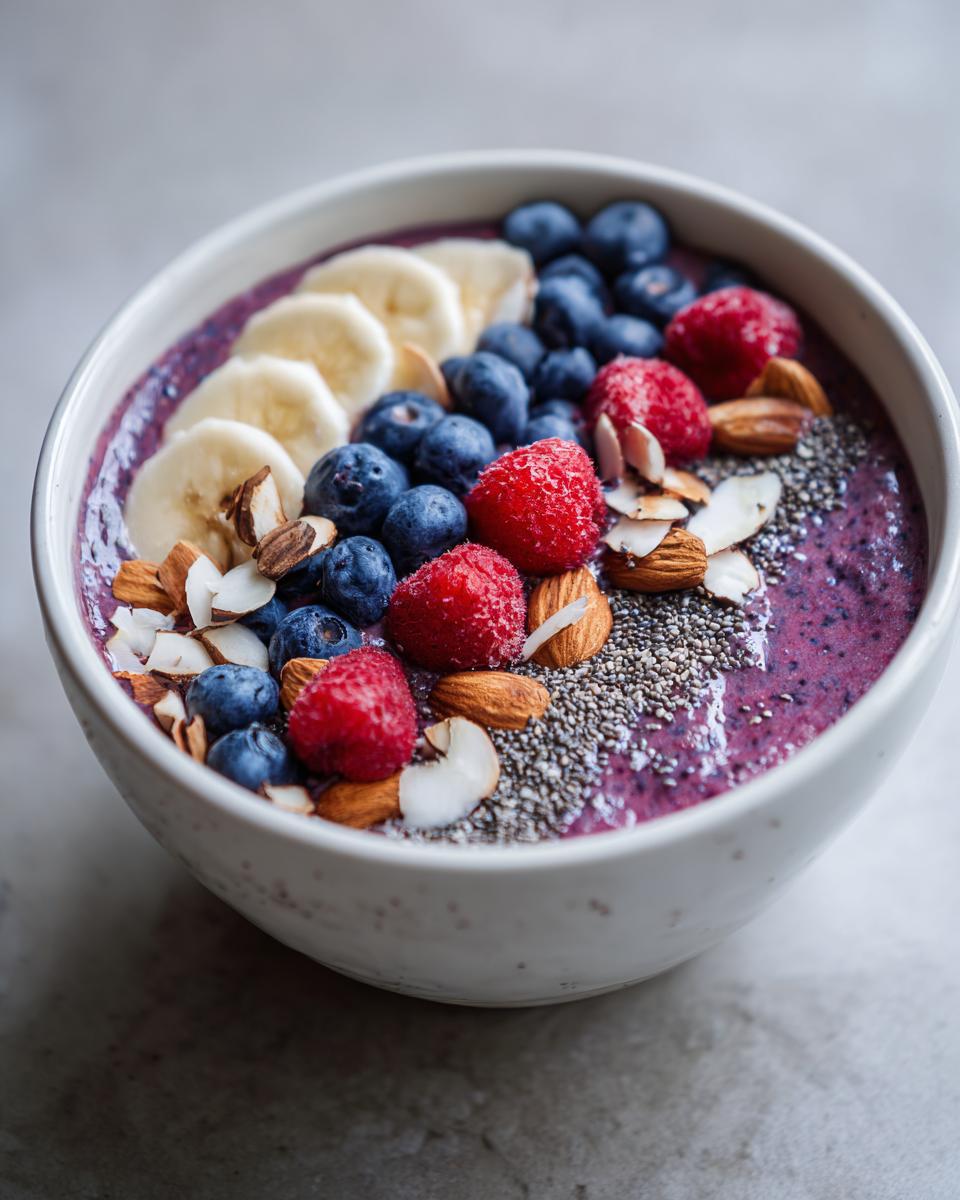 A vibrant weight loss smoothie bowl topped with blueberries, raspberries, banana slices, almonds, and chia seeds.