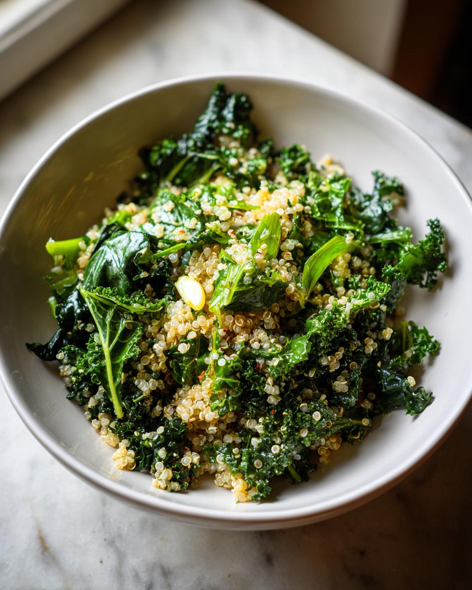 A close-up of a white bowl filled with a vibrant Evergreen 2024 kale and quinoa salad, seasoned with red pepper flakes.