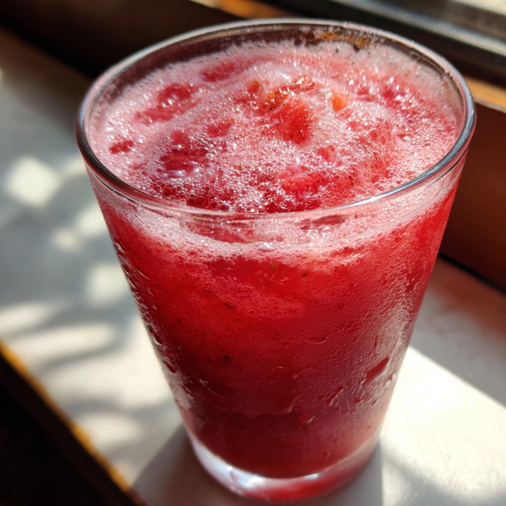 A close-up of a glass filled with frothy strawberry acai peach juice, perfect for a quick save.