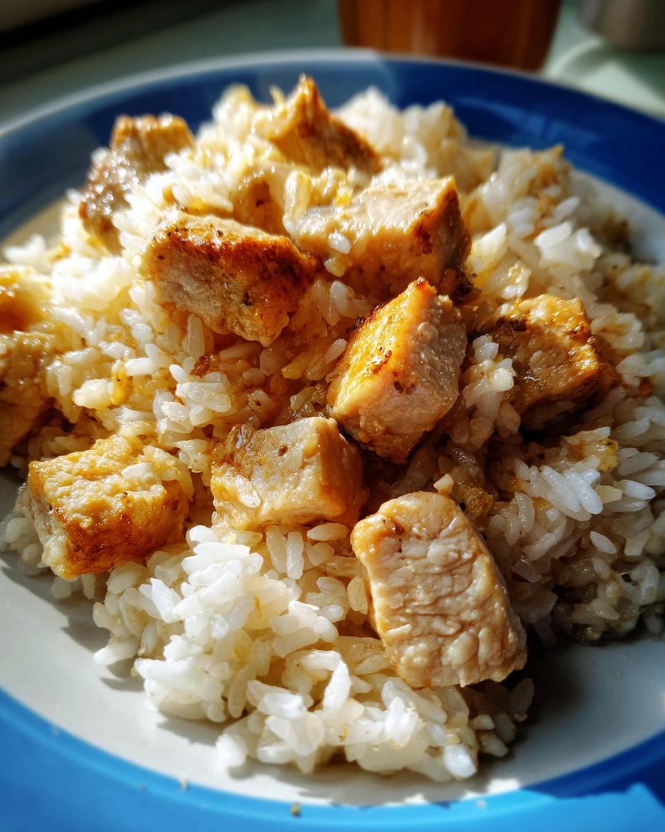 Close-up of a plate filled with fluffy white rice and topped with bite-sized pieces of seasoned, pan-fried chicken.
