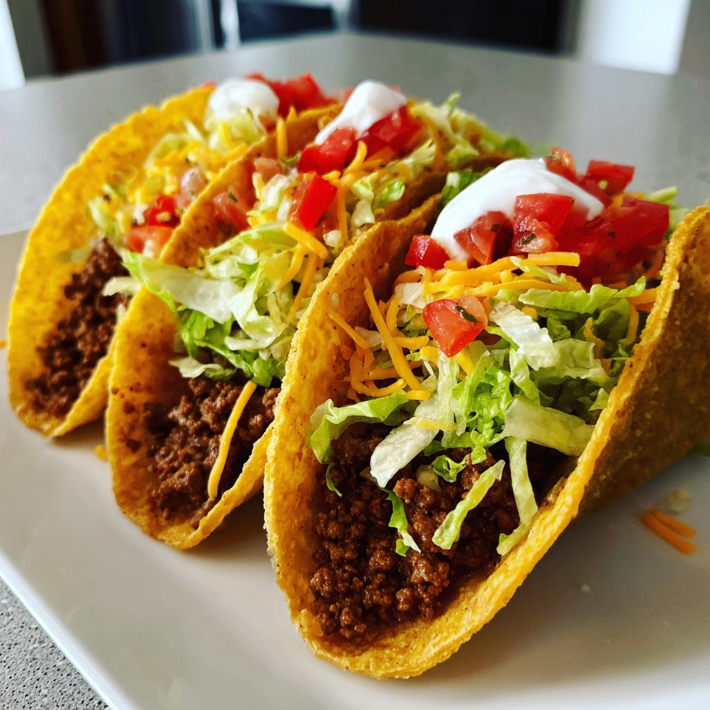 Three classic ground beef tacos loaded with shredded lettuce, cheese, diced tomatoes, and sour cream. A perfect addition to your taco recipes.