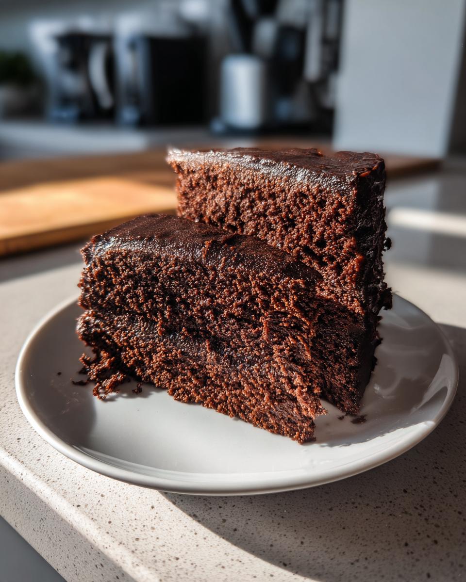 Two slices of rich chocolate cake stacked on a white plate in natural light