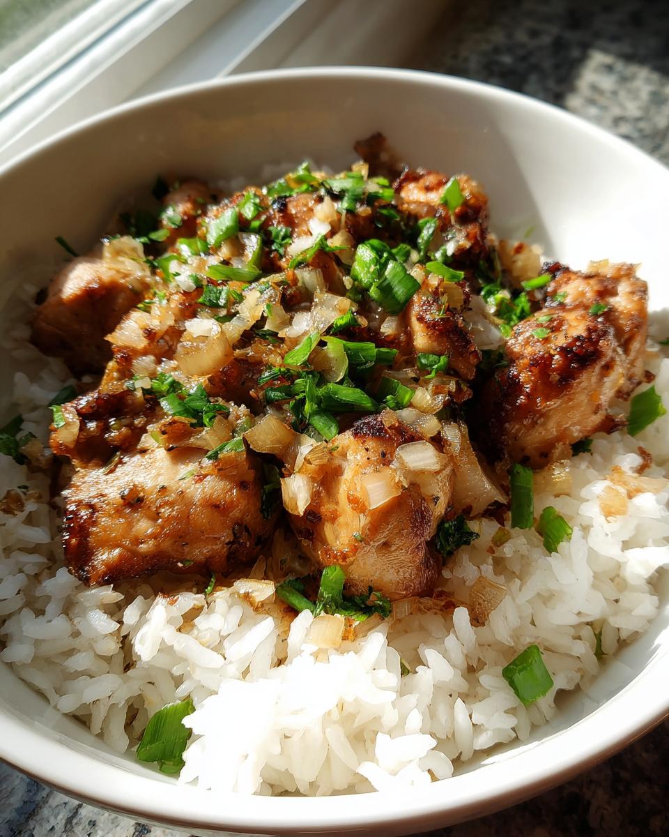 Bowl of cooked white rice topped with seasoned chicken chunks and chopped green herbs.