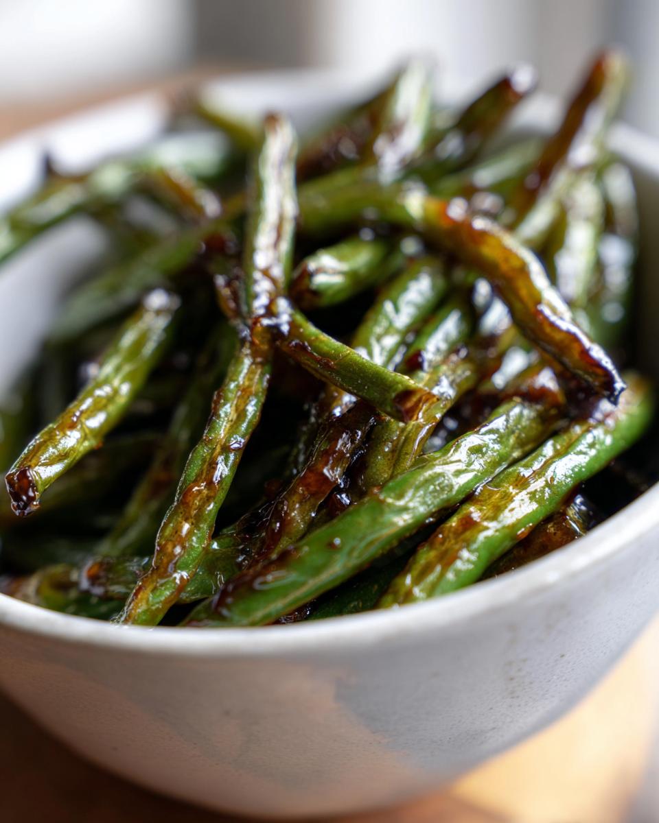 Close-up of honey garlic roasted green beans with caramelized glaze in a white bowl.