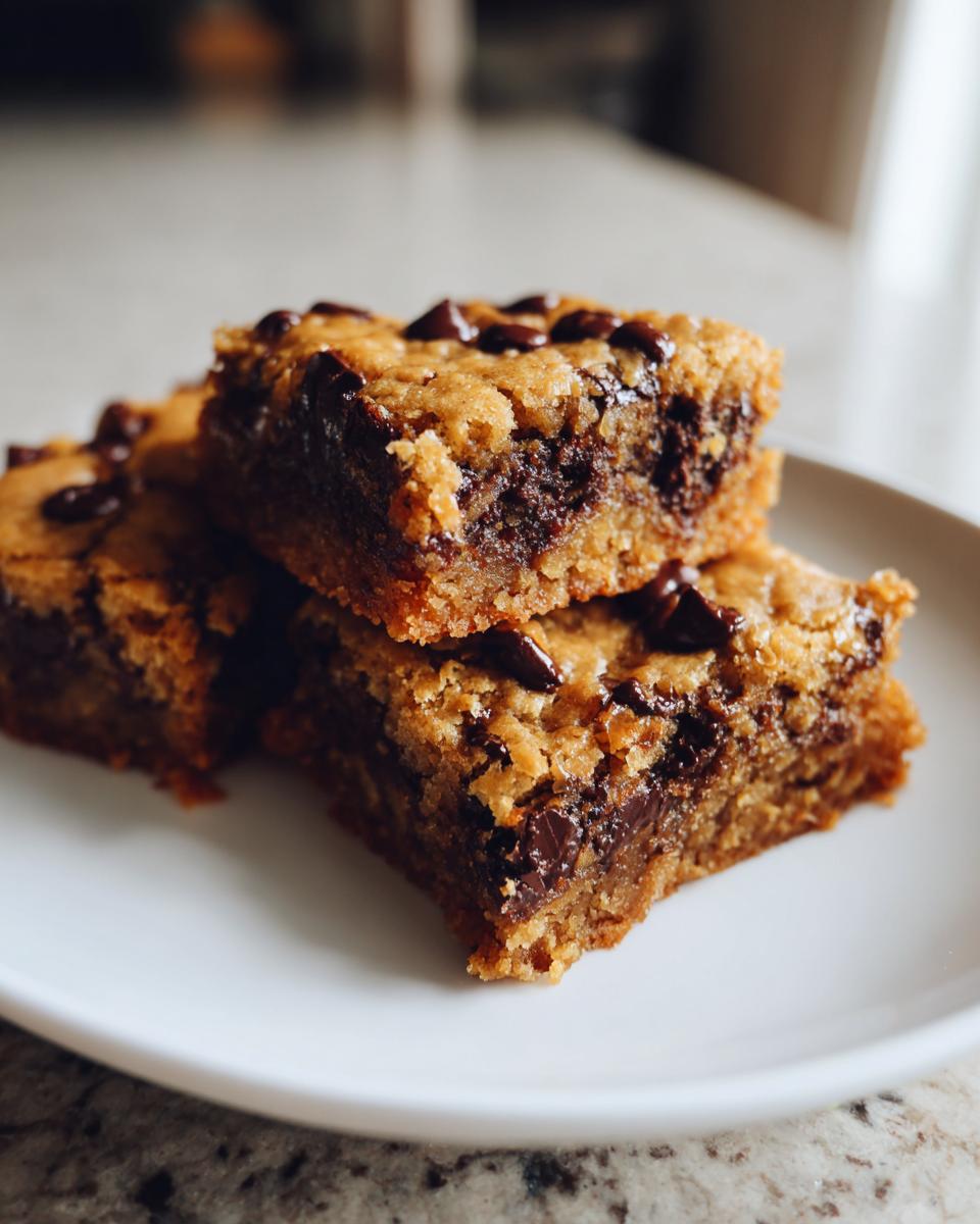 Close-up of three peanut butter chocolate chip blondies stacked on a white plate