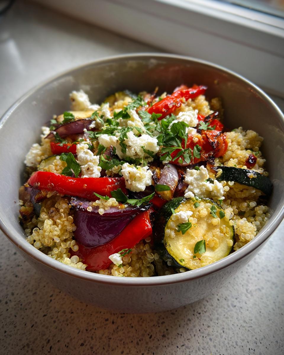 Bowl of quinoa salad with roasted red peppers, zucchini, red onions, feta, and fresh herbs.