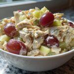 Bowl of chicken salad with grapes and Greek yogurt, featuring shredded chicken, red grapes, and celery.
