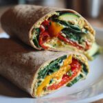 Close-up of a roasted vegetable hummus wrap for lunch cut in half showing colorful veggies and spinach inside.