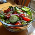 Fresh simple garden salad with homemade vinaigrette in a clear glass bowl on wooden table