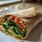 Close-up of a turkey avocado wrap with spinach and tomato on a white plate