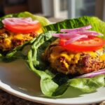 Two turkey burger lettuce wraps with cheese topped with tomato slices and red onion on a white plate.