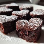 Close-up of valentines heart shaped brownie bites dusted with powdered sugar on a white plate.