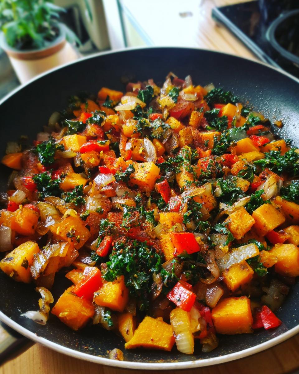 Colorful veggie packed hash with sweet potatoes, kale, onions, and red peppers in a black skillet.