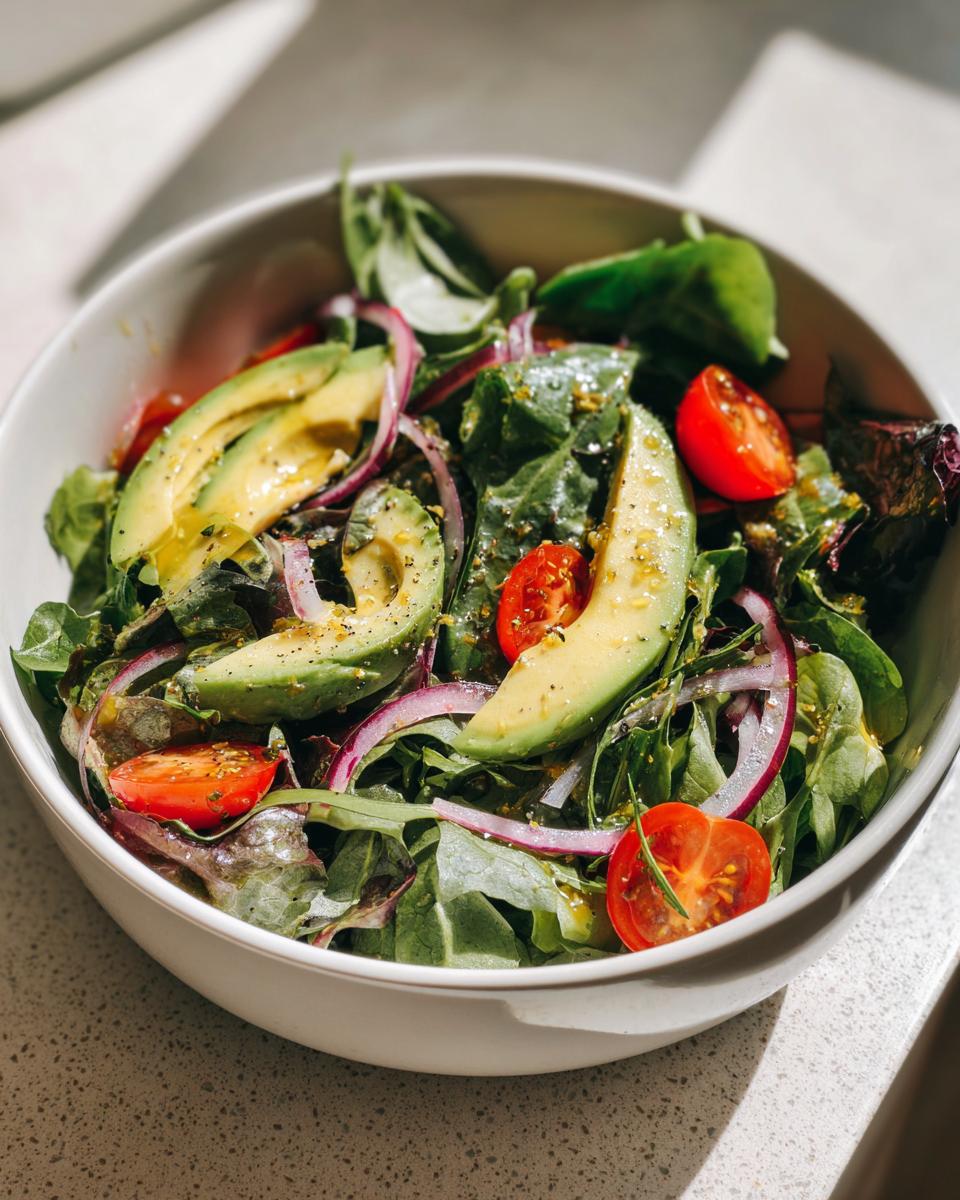 Bowl of fresh salad with avocado slices, cherry tomatoes, red onion, and leafy greens for light spring lunches