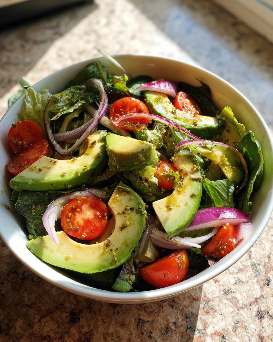 Bowl of fresh salad with avocado slices, cherry tomatoes, red onion, and leafy greens for light spring lunches