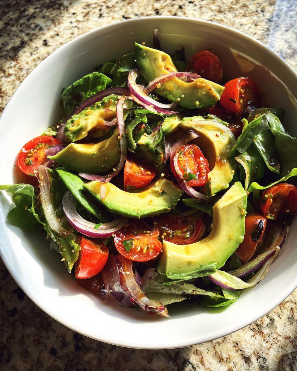 Bowl of fresh salad with avocado slices, cherry tomatoes, red onion, and leafy greens for light spring lunches.