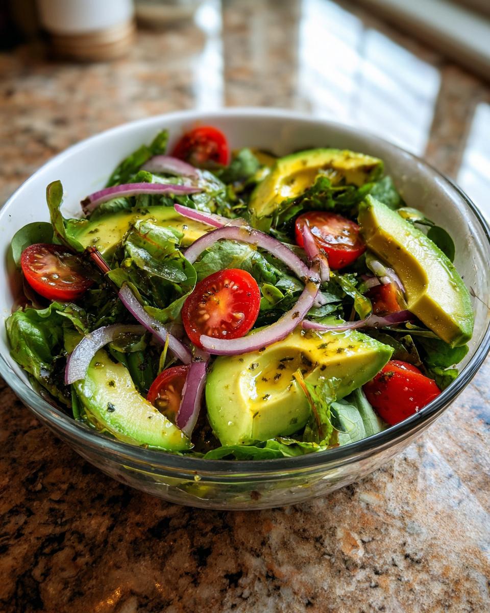Bowl of fresh avocado, cherry tomatoes, red onion, and leafy greens salad for light spring lunches.