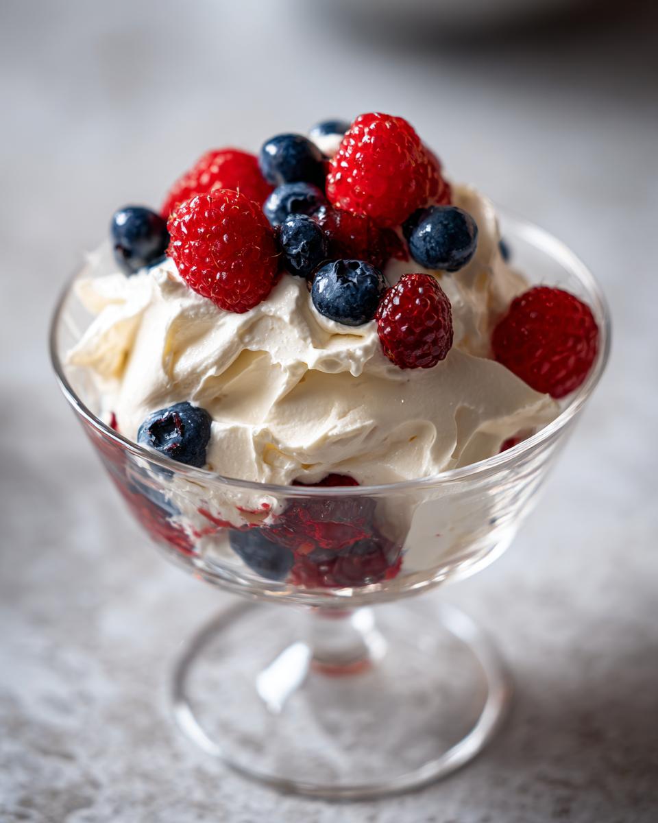 Glass dessert dish with whipped cream topped with fresh raspberries and blueberries, a spring party dessert recipe