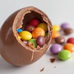 A broken breakable chocolate egg filled with colorful candy-coated chocolates spilling out.