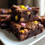 Stack of moist Cadbury mini egg brownies with colorful candy pieces on a white plate.
