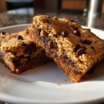 Two chocolate chip cookie bars stacked on a white plate with visible chocolate chips
