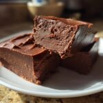 Close-up of three thick pieces of chocolate fudge recipe stacked on a white plate.