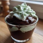 Glass cup filled with layered chocolate mint dessert topped with green whipped cream.