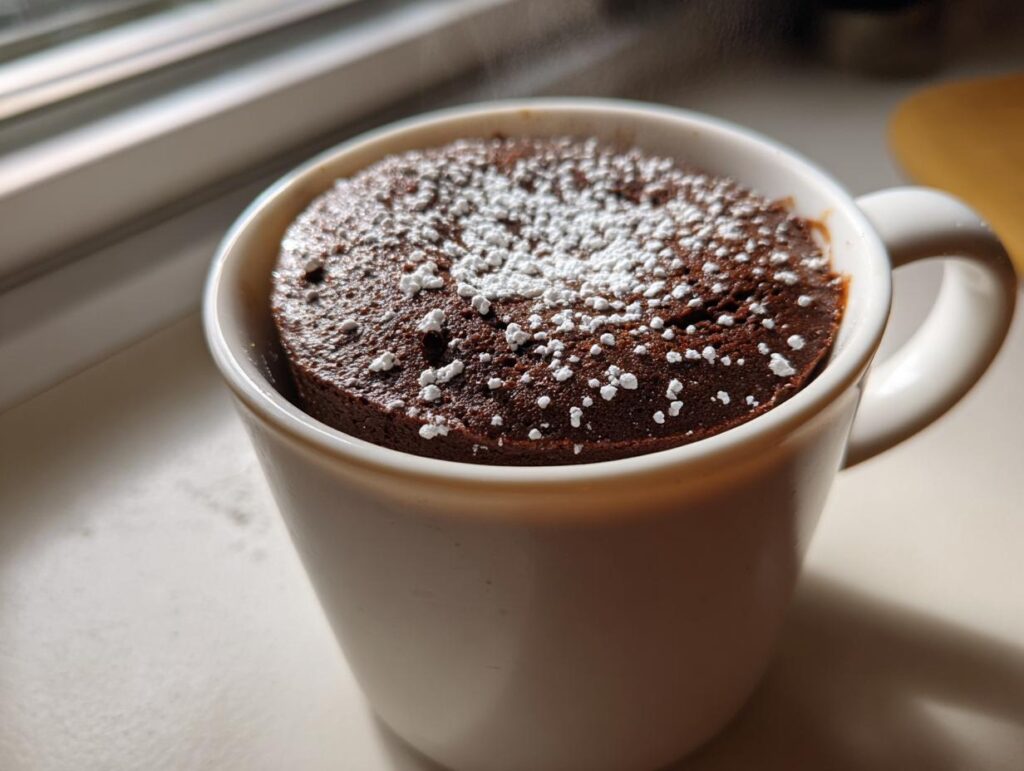 Close-up of a chocolate mug cake topped with powdered sugar in a white mug, an easy dessert recipes idea.