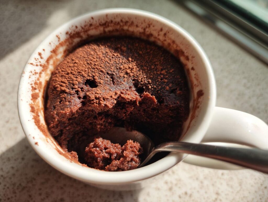 Close-up of a chocolate mug cake with a spoon inside, showcasing a quick dessert recipe.