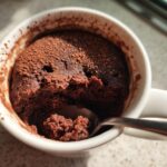 Close-up of a chocolate mug cake with a spoon inside, showcasing a quick dessert recipe.