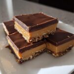 Stack of chocolate peanut butter desserts with layered chocolate, peanut butter, and crust.