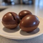 Three chocolate smash eggs on a white plate, one cracked open.