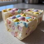 Close-up of three pieces of white Easter fudge recipes with pastel candy decorations on a plate.
